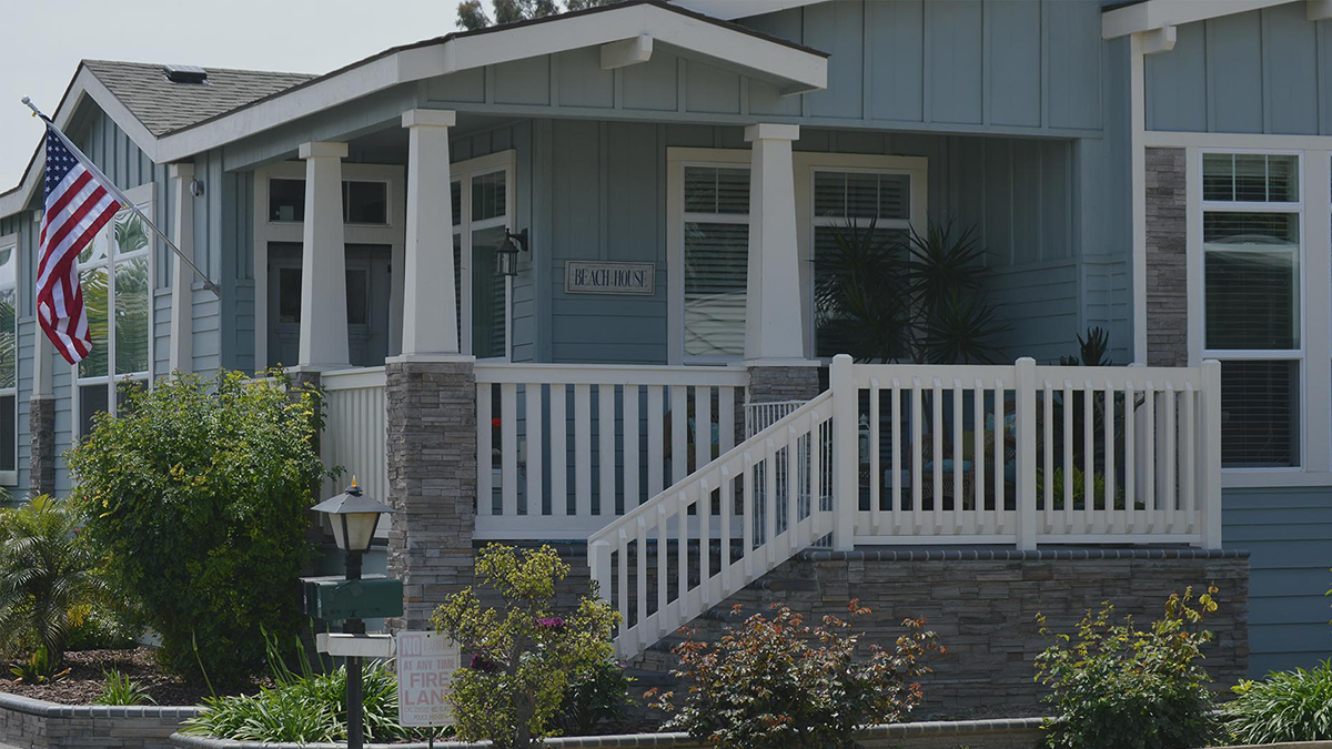 Blue manufactured home with porch that has white posts and with fence like railing.